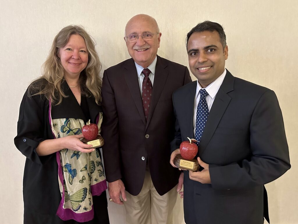 Three individuals, two men and a woman pose with two of them holding awards