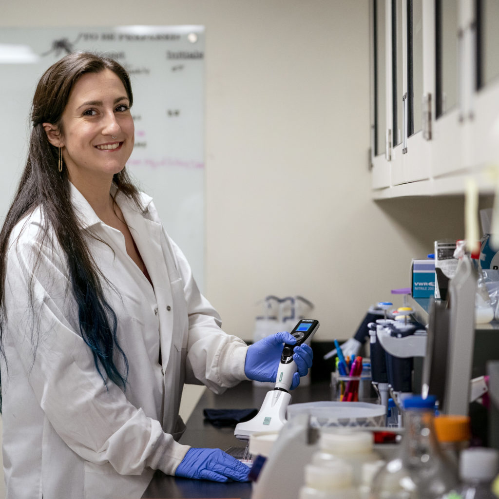 student wearing labcoat and smiling while standing next to counter in lab
