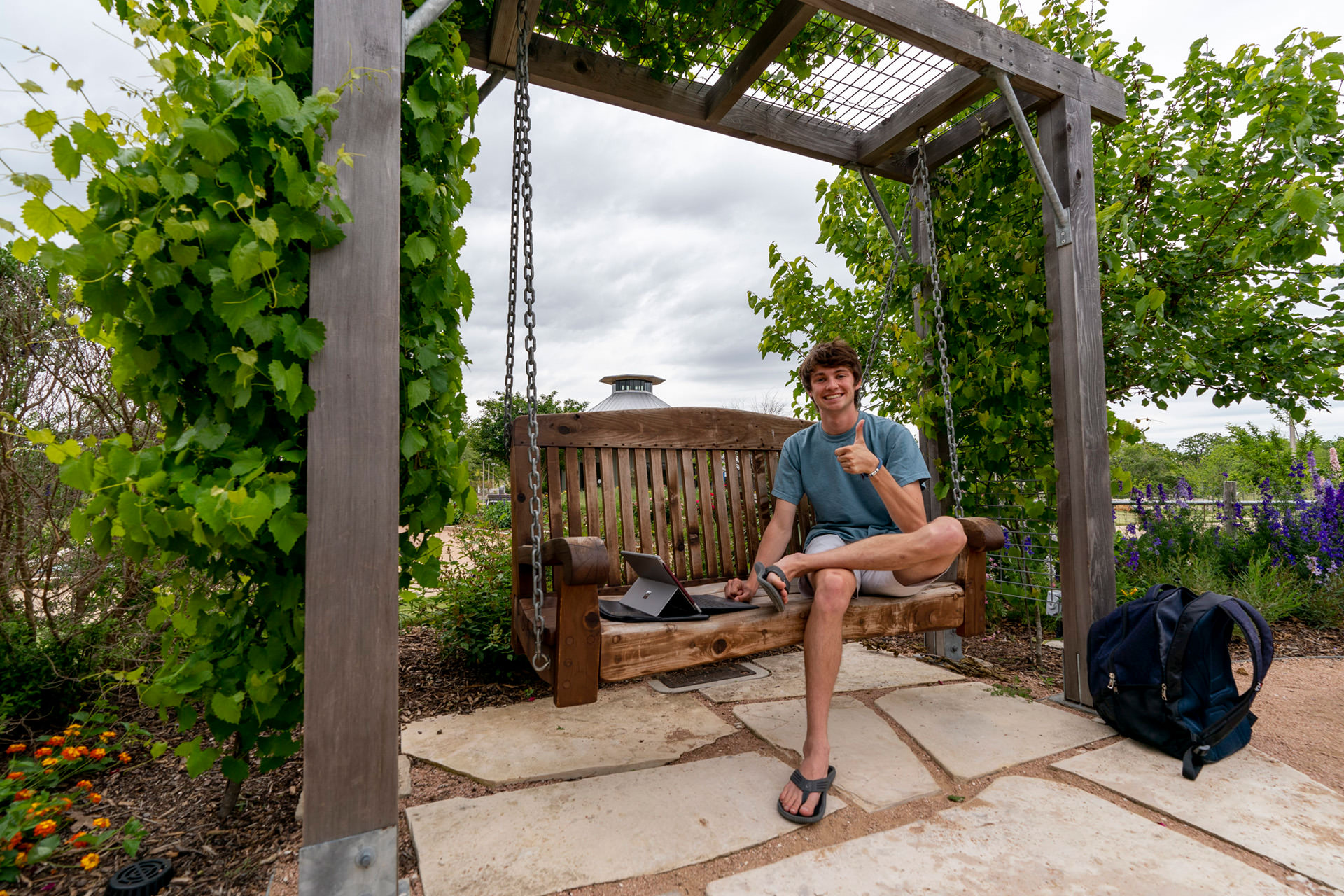 Student sitting at bench at Aggie Gardens using a computer.