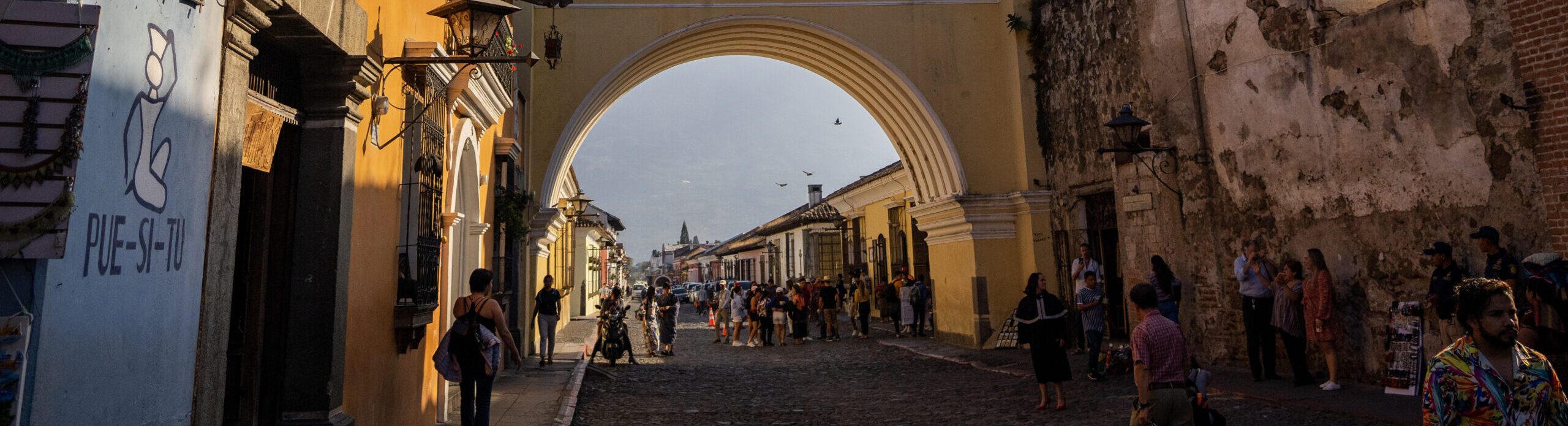 Yellow building with an arched wall, people seen in the background walking down the street.